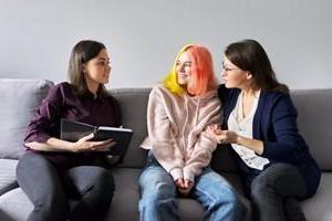 Teen girl with dyed hair with woman on couch talking with counselor